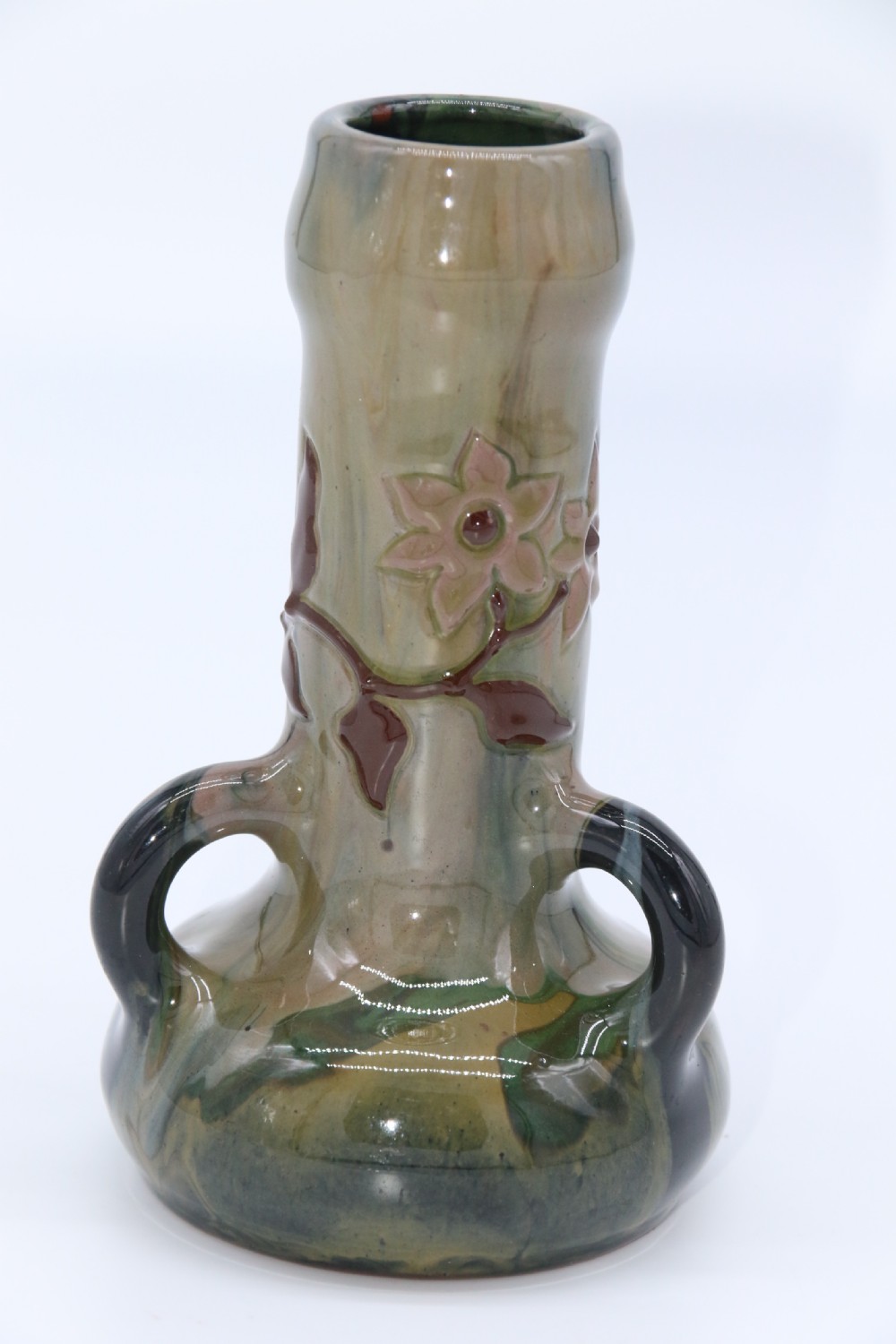 A green and brown glazed earthenware ceramic vase featuring three handles and raised slipware floral decoration. View X
