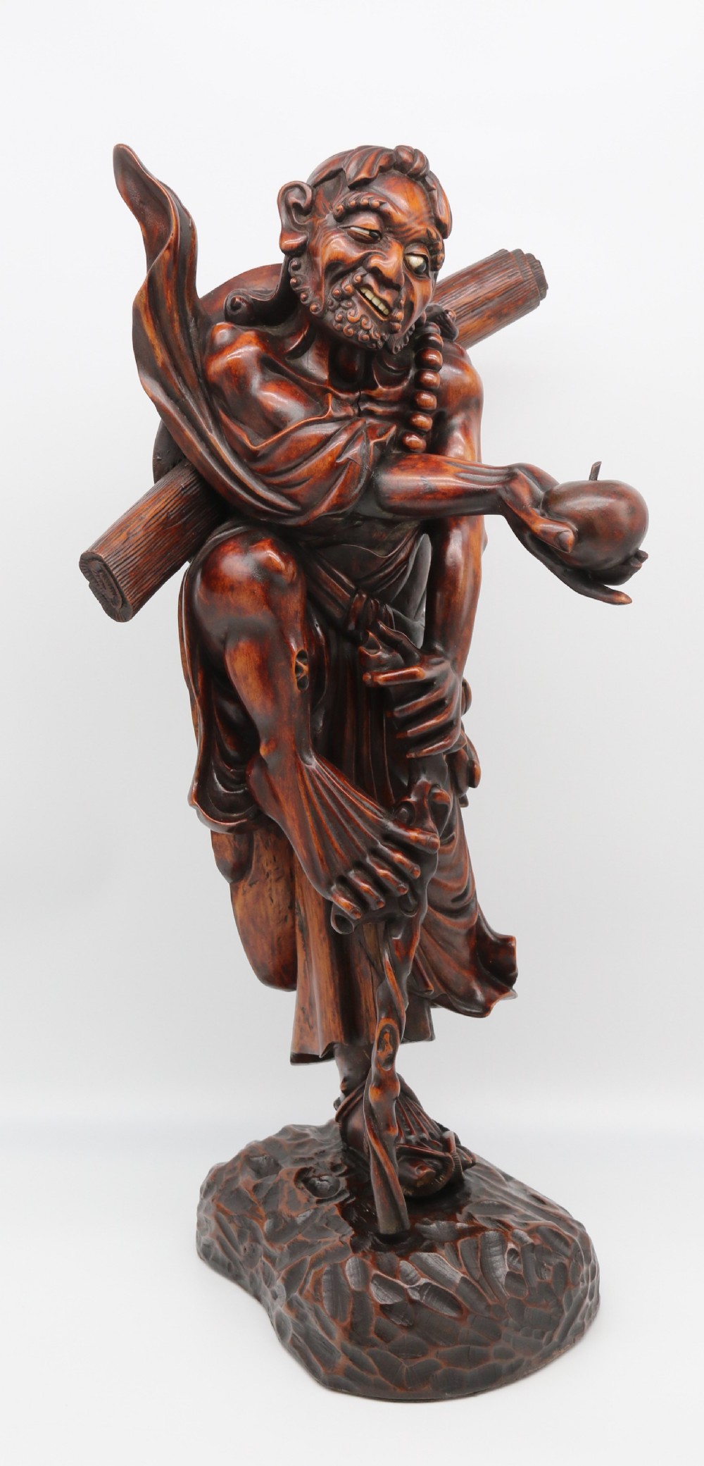 A late 19th-century Japanese Meiji period carved hardwood okimono depicting a standing male figure with a staff, scroll, and fruit on a textured base.