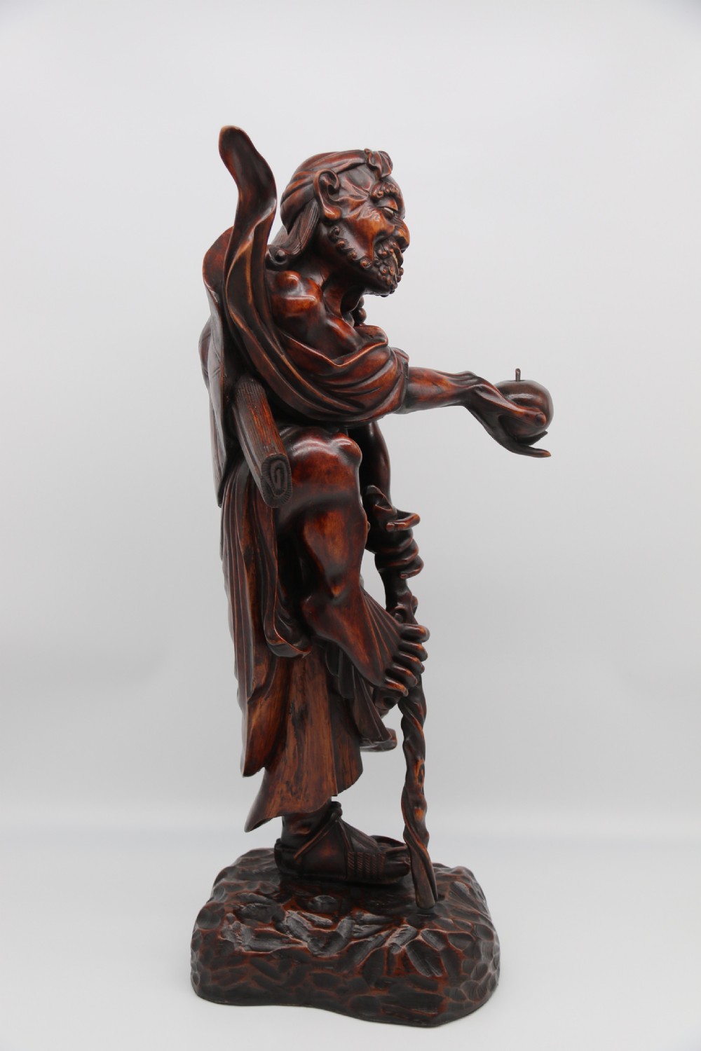 A late 19th-century Japanese Meiji period carved hardwood okimono depicting a standing male figure with a staff, scroll, and fruit on a textured base. View II