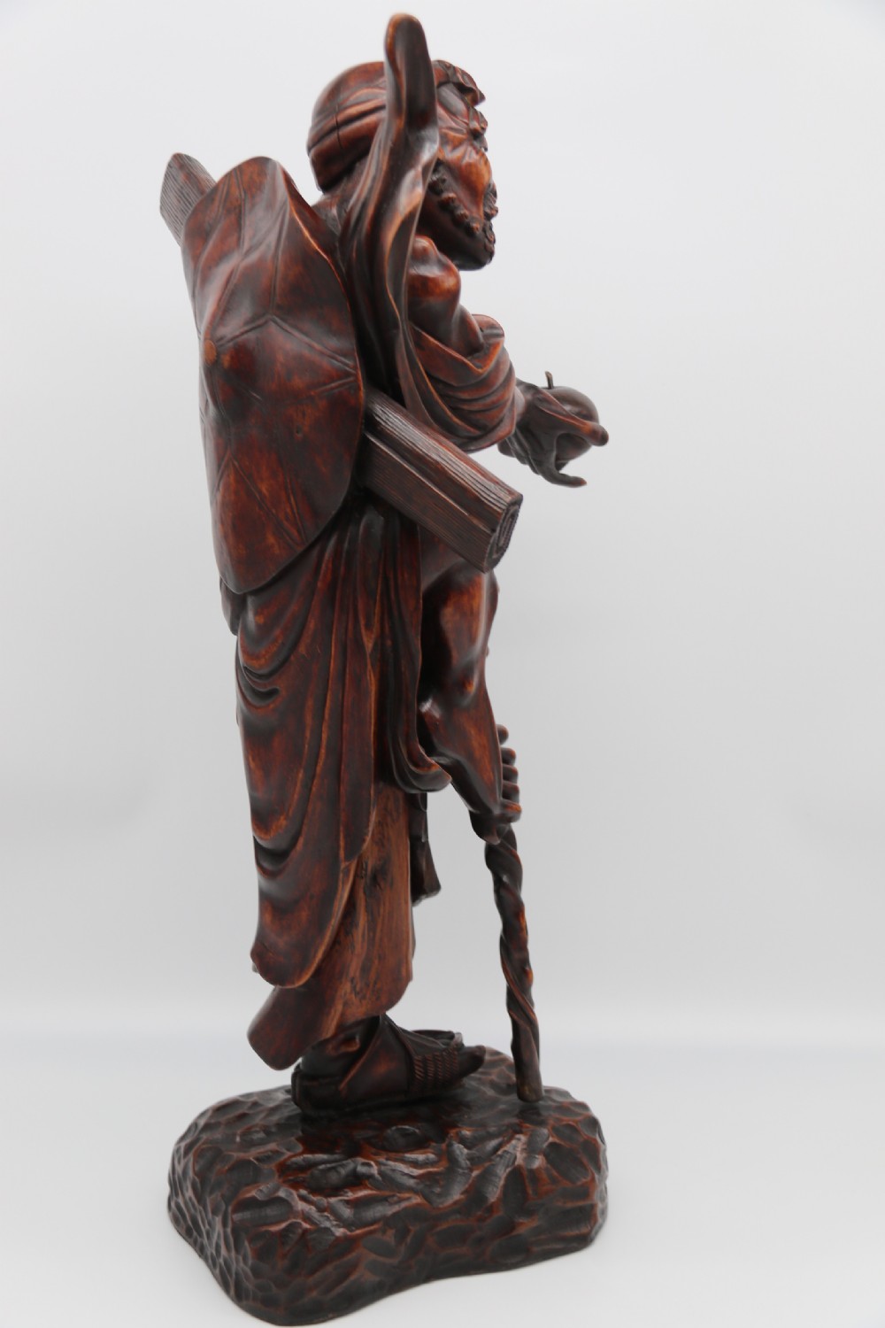 A late 19th-century Japanese Meiji period carved hardwood okimono depicting a standing male figure with a staff, scroll, and fruit on a textured base. View III