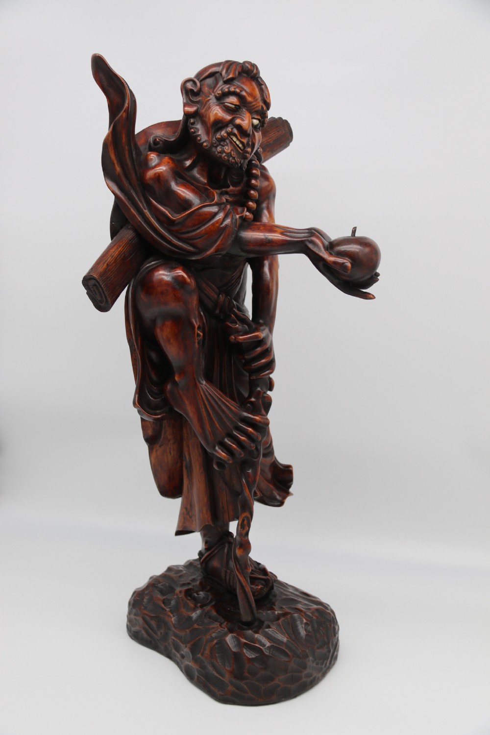 A late 19th-century Japanese Meiji period carved hardwood okimono depicting a standing male figure with a staff, scroll, and fruit on a textured base. View IV