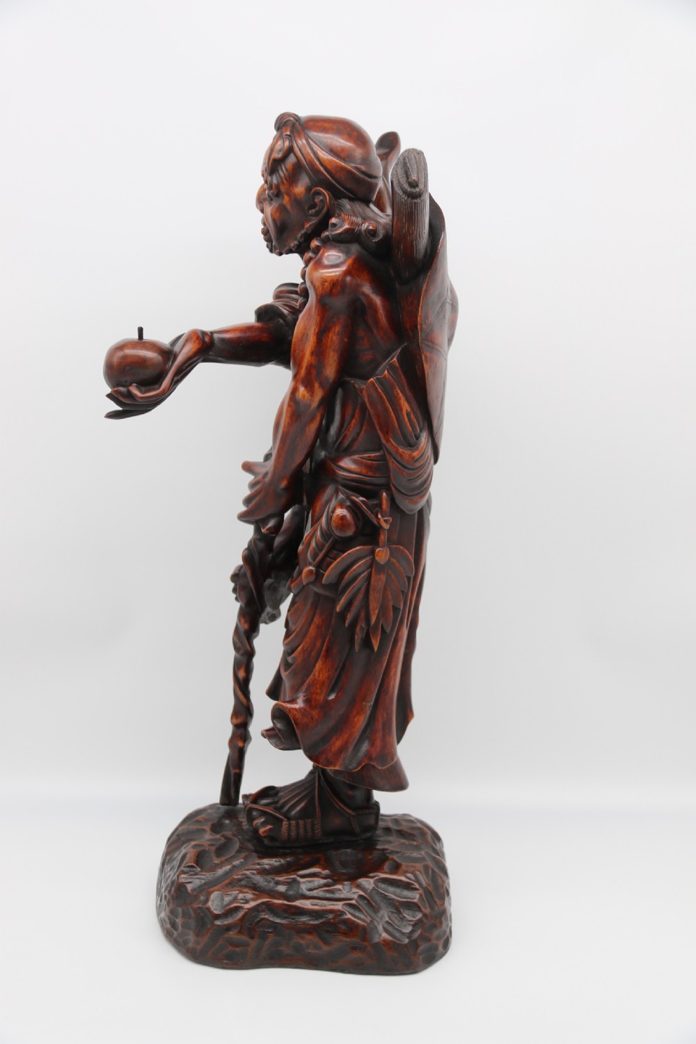 A late 19th-century Japanese Meiji period carved hardwood okimono depicting a standing male figure with a staff, scroll, and fruit on a textured base. View VIII