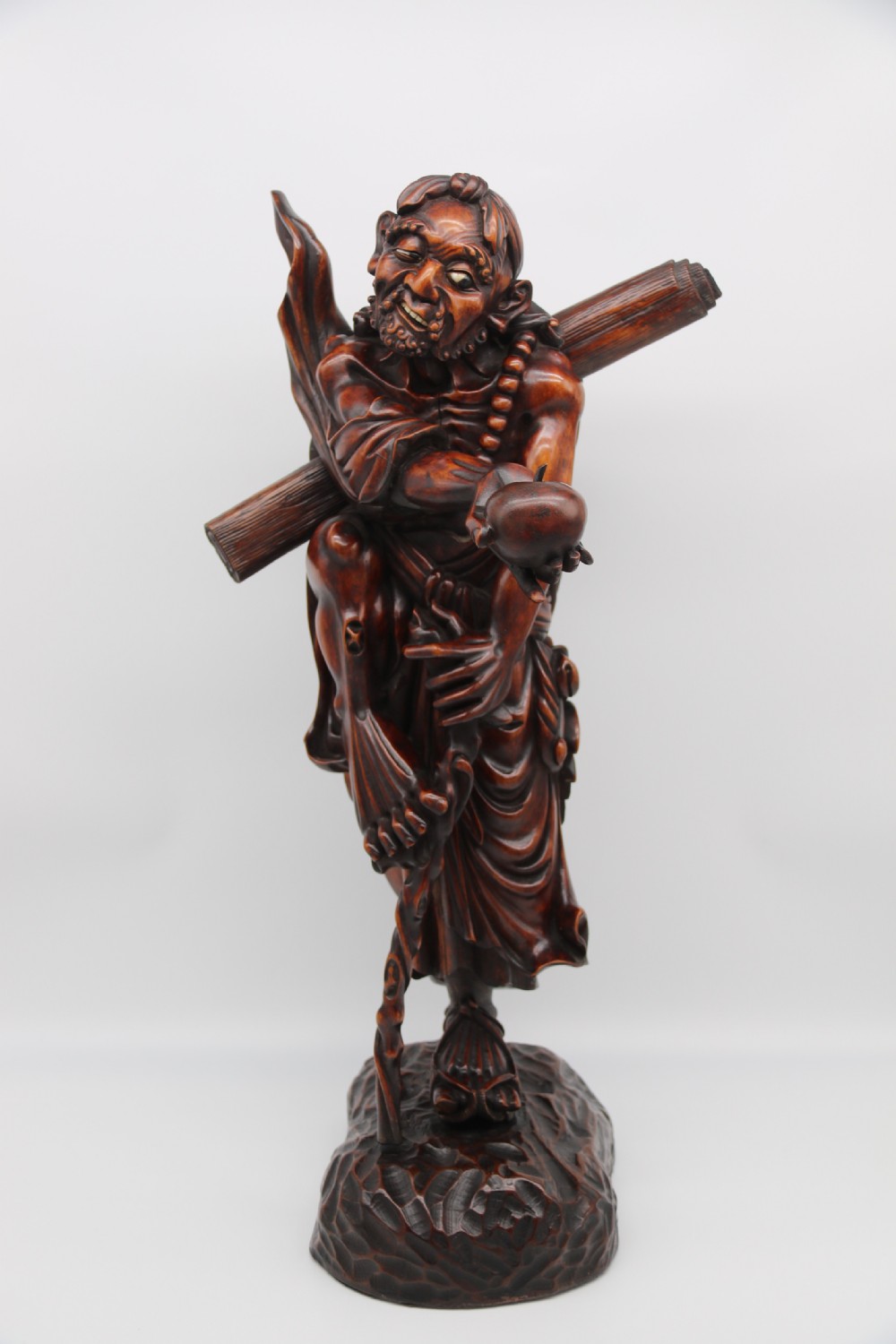 A late 19th-century Japanese Meiji period carved hardwood okimono depicting a standing male figure with a staff, scroll, and fruit on a textured base. View X