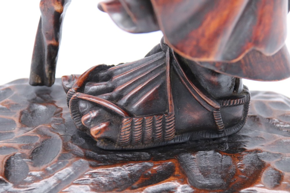 A late 19th-century Japanese Meiji period carved hardwood okimono depicting a standing male figure with a staff, scroll, and fruit on a textured base. View XVII