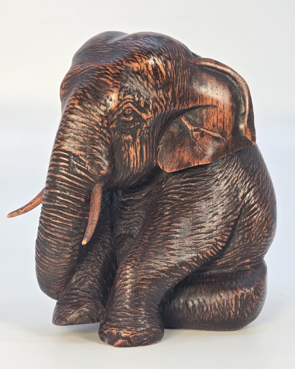 A hand-carved dark hardwood sculpture depicting a seated elephant with textured skin detailing and inset tusks.