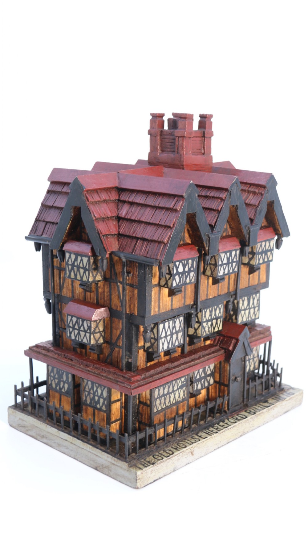 A hand-crafted matchstick model of a three-storey Tudor style half-timbered house featuring red gabled roof tiles, black timber details, and leaded window patterns on a rectangular wooden base.