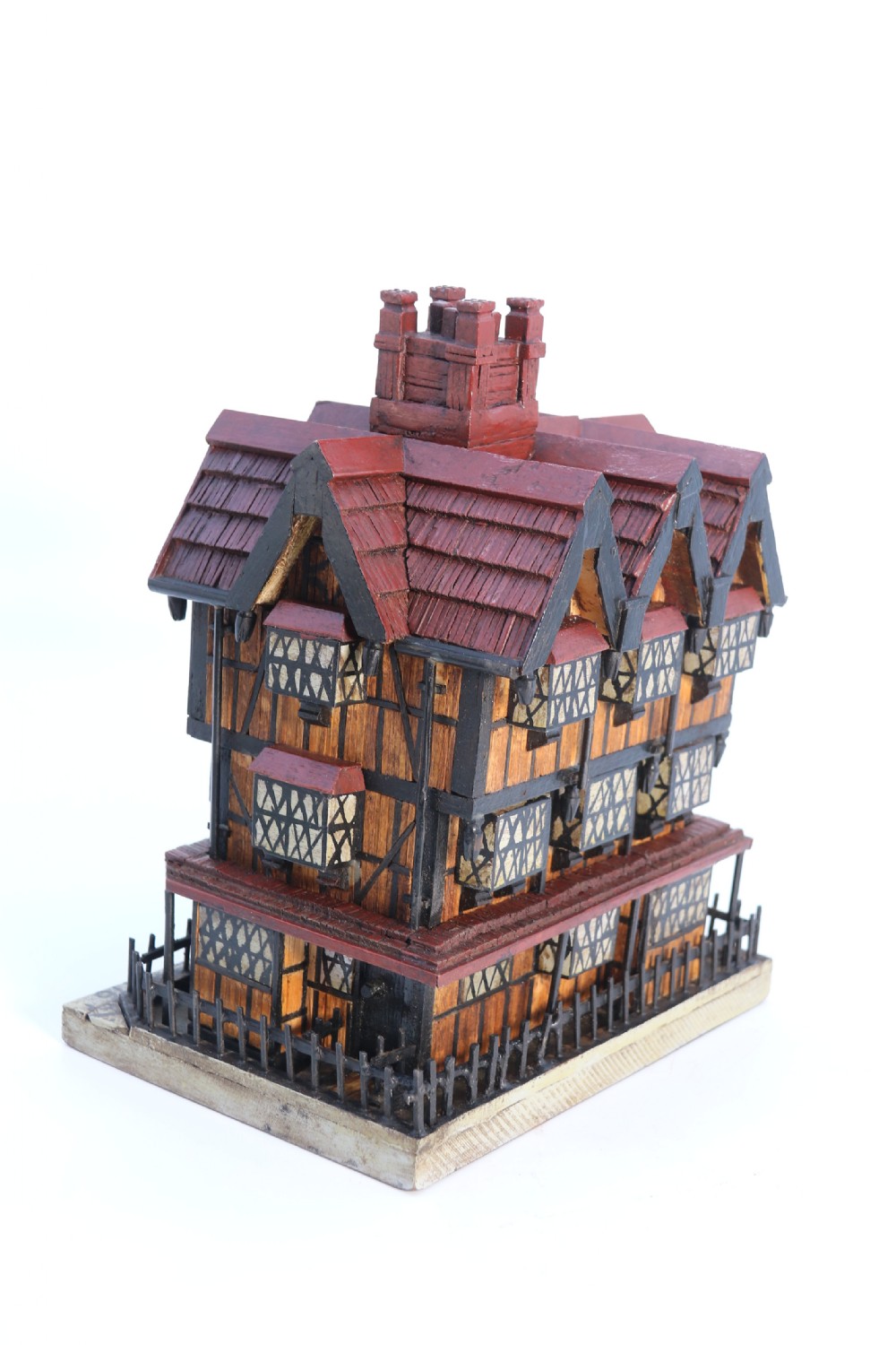 A hand-crafted matchstick model of a three-storey Tudor style half-timbered house featuring red gabled roof tiles, black timber details, and leaded window patterns on a rectangular wooden base. View IV