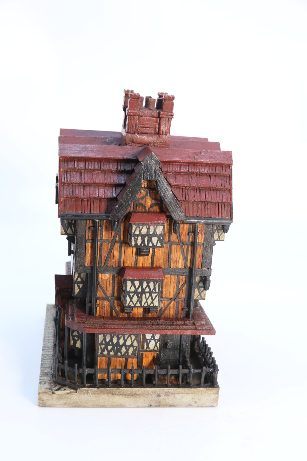 A hand-crafted matchstick model of a three-storey Tudor style half-timbered house featuring red gabled roof tiles, black timber details, and leaded window patterns on a rectangular wooden base. View V