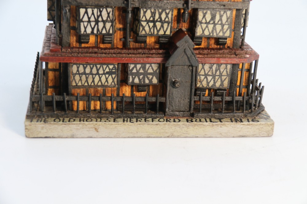 A hand-crafted matchstick model of a three-storey Tudor style half-timbered house featuring red gabled roof tiles, black timber details, and leaded window patterns on a rectangular wooden base. View VIII