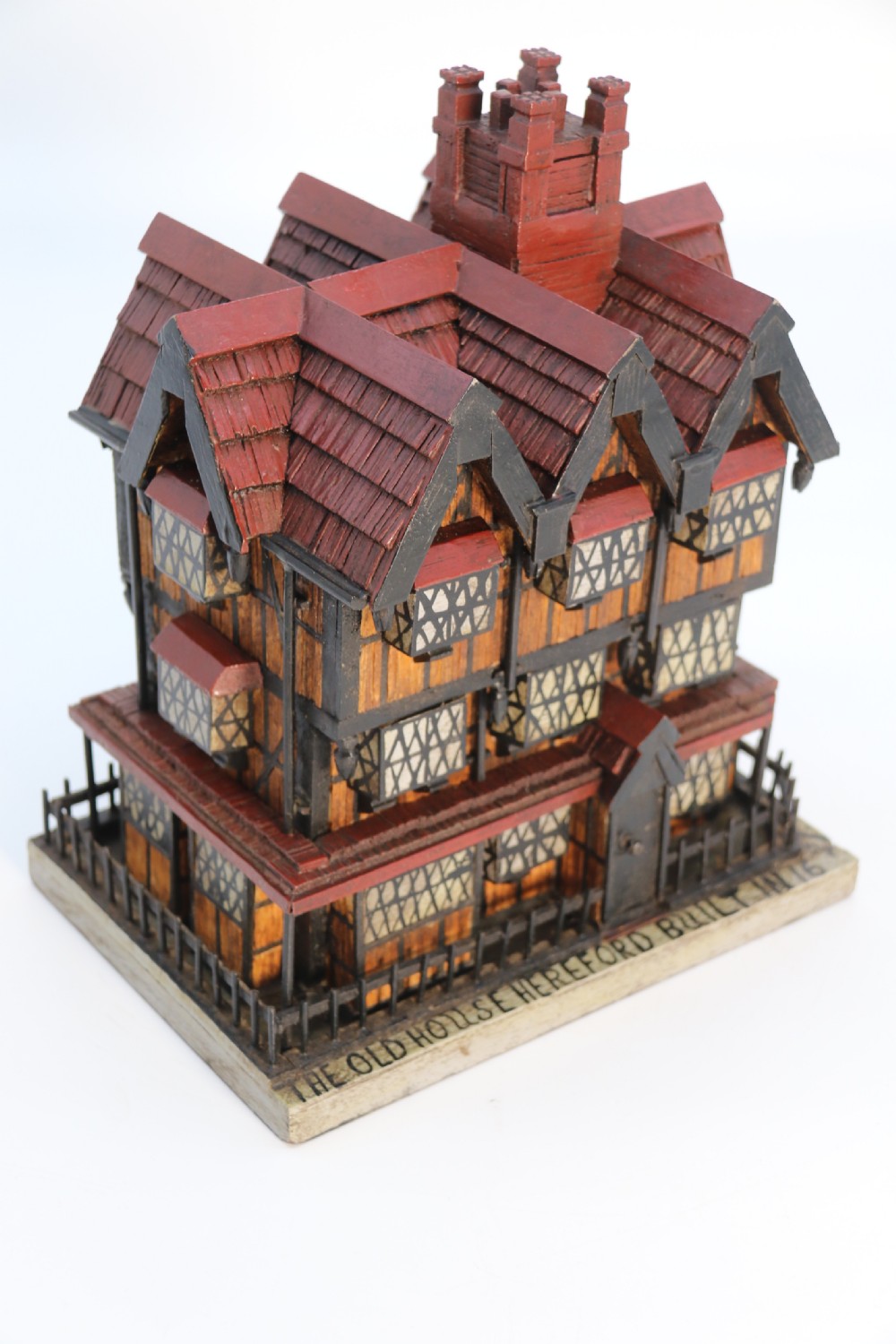 A hand-crafted matchstick model of a three-storey Tudor style half-timbered house featuring red gabled roof tiles, black timber details, and leaded window patterns on a rectangular wooden base. View XIII