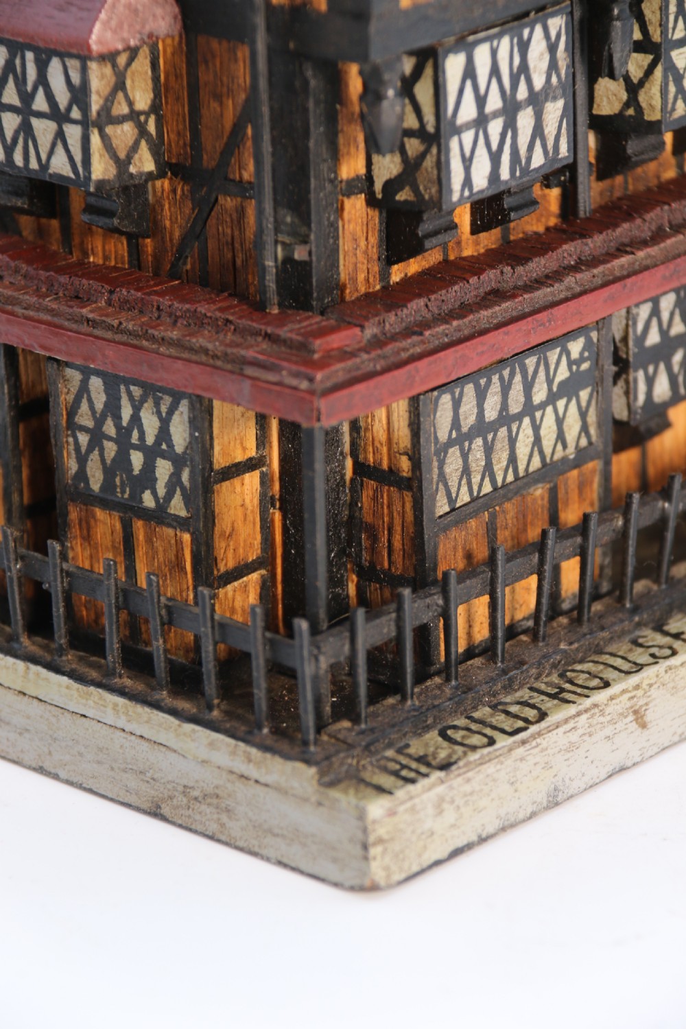 A hand-crafted matchstick model of a three-storey Tudor style half-timbered house featuring red gabled roof tiles, black timber details, and leaded window patterns on a rectangular wooden base. View XIV