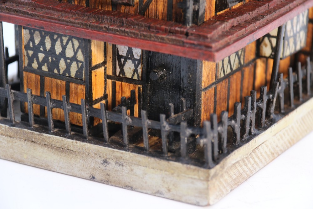 A hand-crafted matchstick model of a three-storey Tudor style half-timbered house featuring red gabled roof tiles, black timber details, and leaded window patterns on a rectangular wooden base. View XVII
