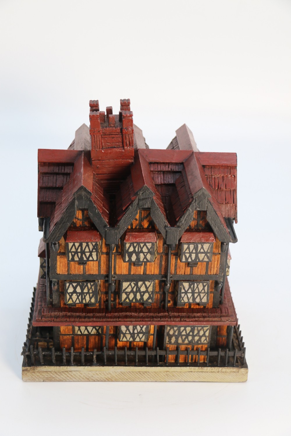A hand-crafted matchstick model of a three-storey Tudor style half-timbered house featuring red gabled roof tiles, black timber details, and leaded window patterns on a rectangular wooden base. View XIX