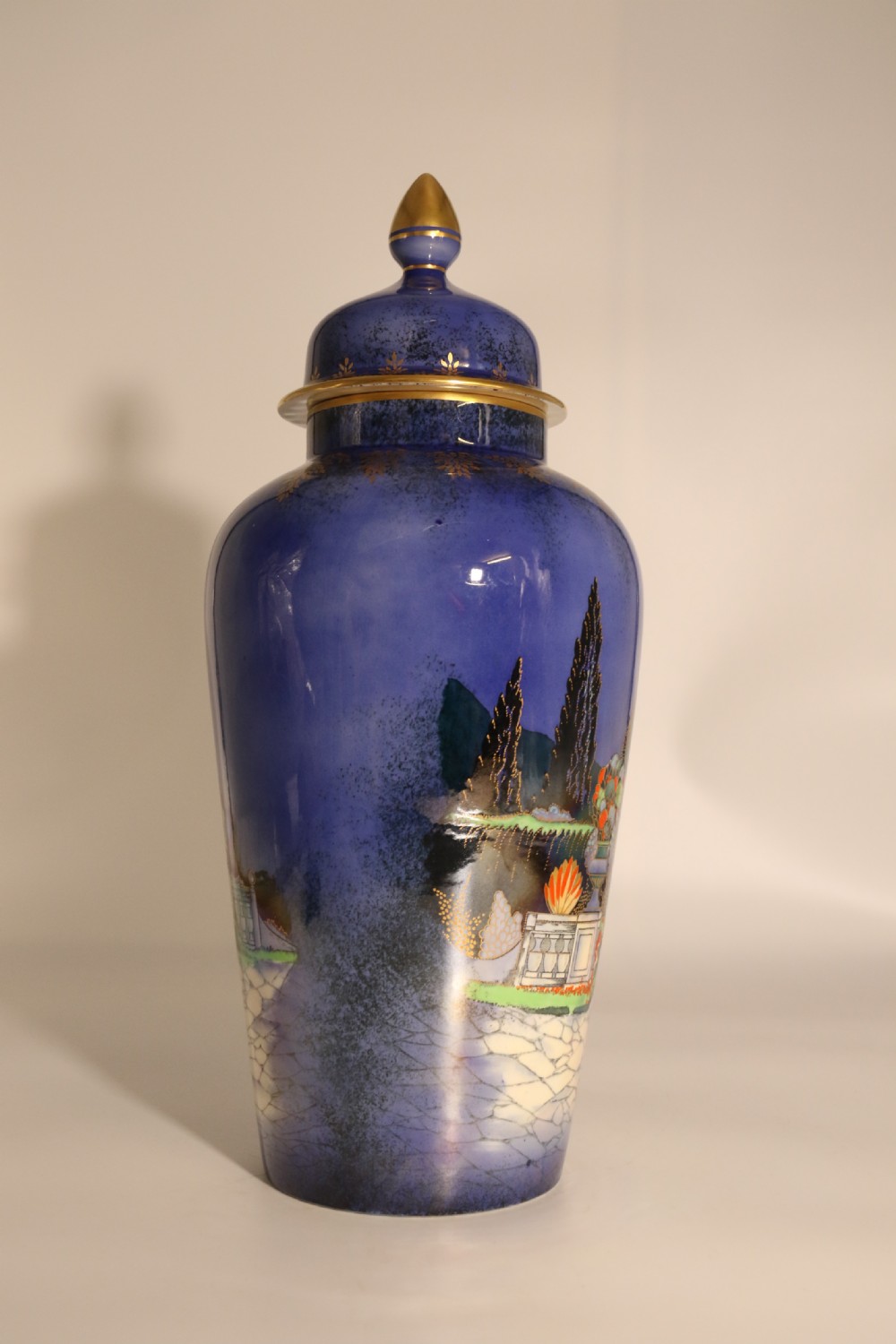 A cobalt blue ceramic lidded vase featuring a painted architectural garden scene with stone arches and gold accents. View VIII