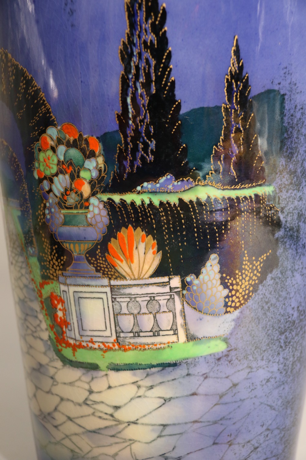 A cobalt blue ceramic lidded vase featuring a painted architectural garden scene with stone arches and gold accents. View XVI