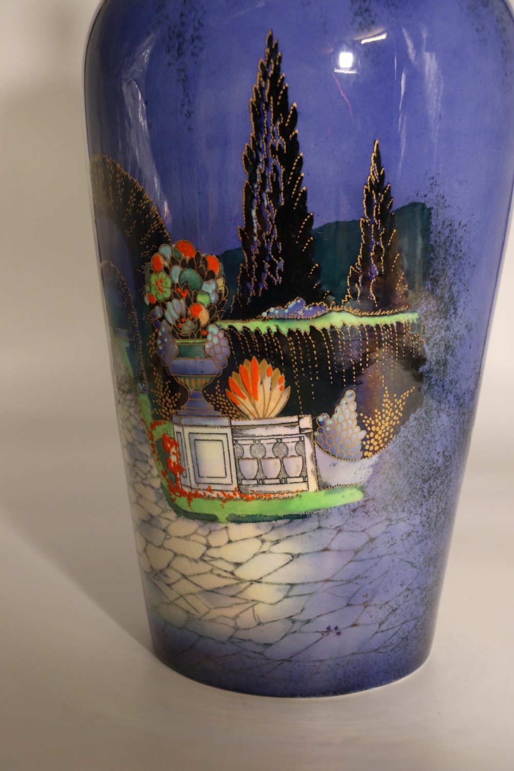 A cobalt blue ceramic lidded vase featuring a painted architectural garden scene with stone arches and gold accents. View XVII