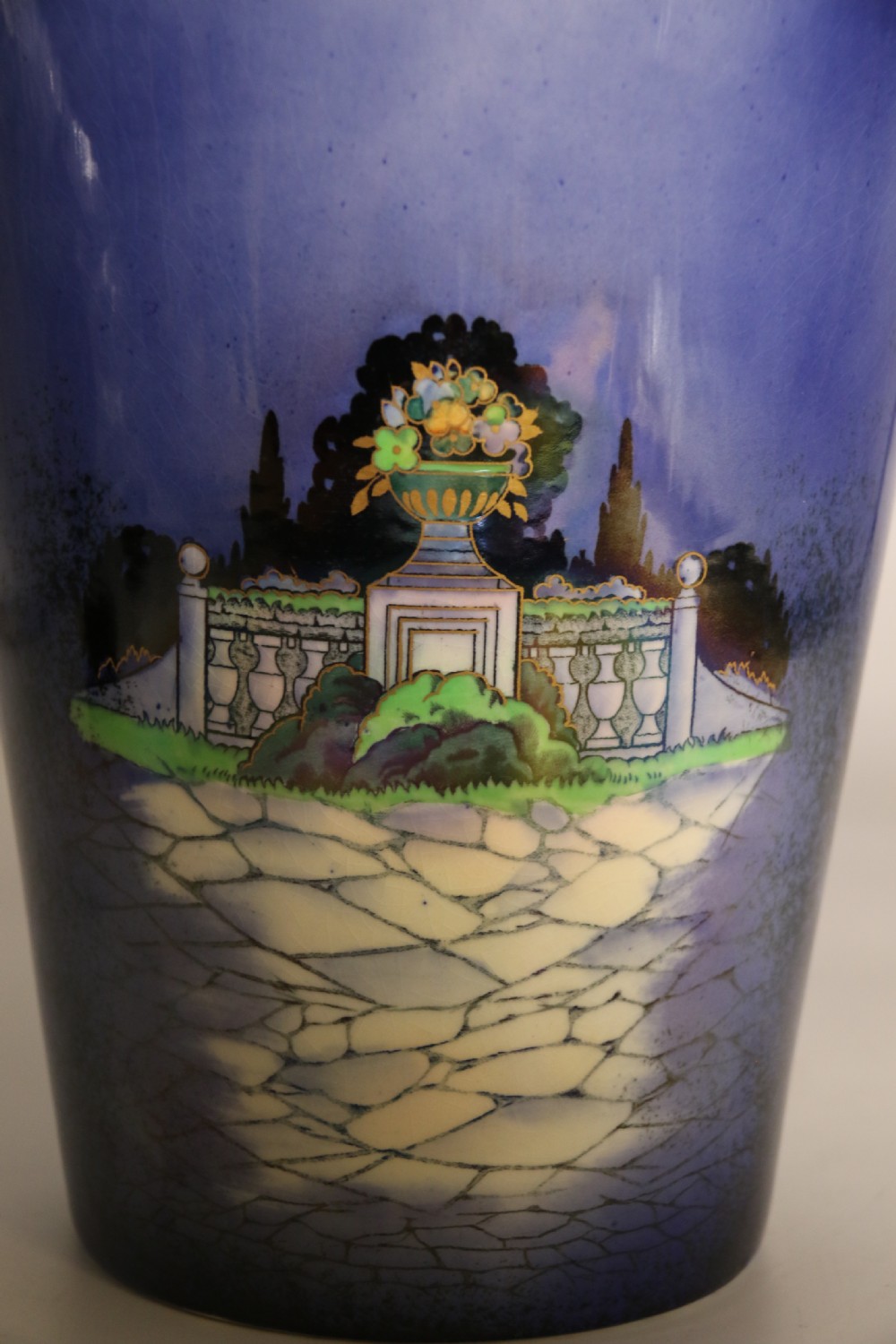A cobalt blue ceramic lidded vase featuring a painted architectural garden scene with stone arches and gold accents. View XVIII