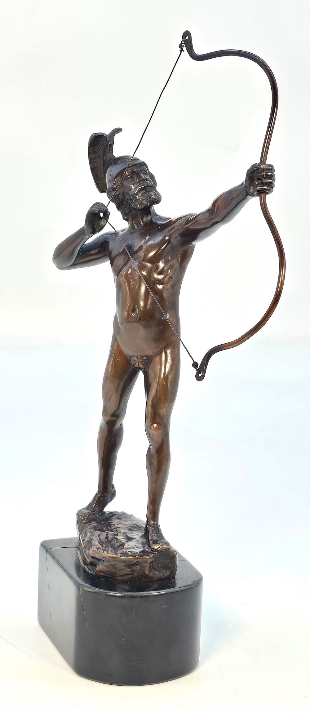 A dark bronze sculpture of a bearded Greek archer wearing a helmet and drawing a bow, mounted on a dark stone base.
