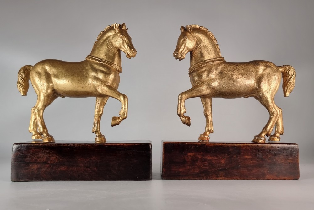 A pair of 19th-century Italian gilt bronze horse sculptures depicted facing each other, mounted on rectangular dark olive wood bases.