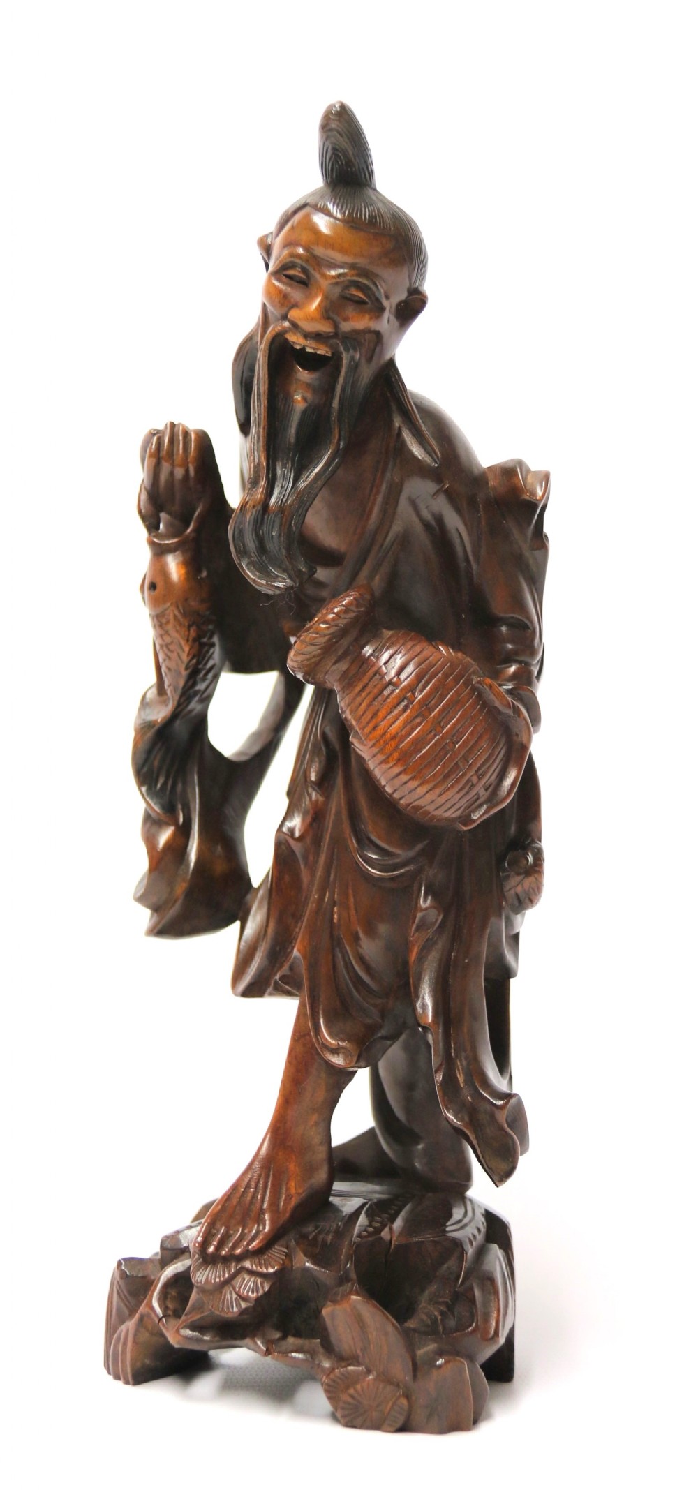 A 19th-century carved dark hardwood figure of a laughing Chinese fisherman holding a fish and a basket trap while standing on a sculpted rock base.