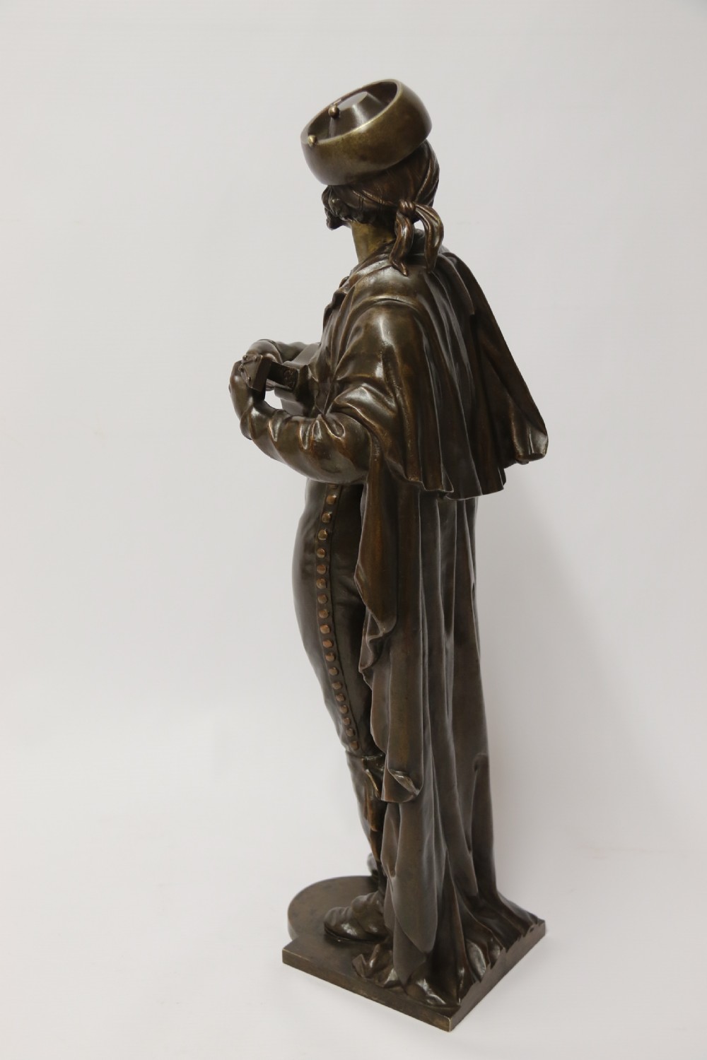 A patinated dark brown bronze sculpture depicting a standing male musician playing a mandolin while wearing a draped coat and headwear. View II