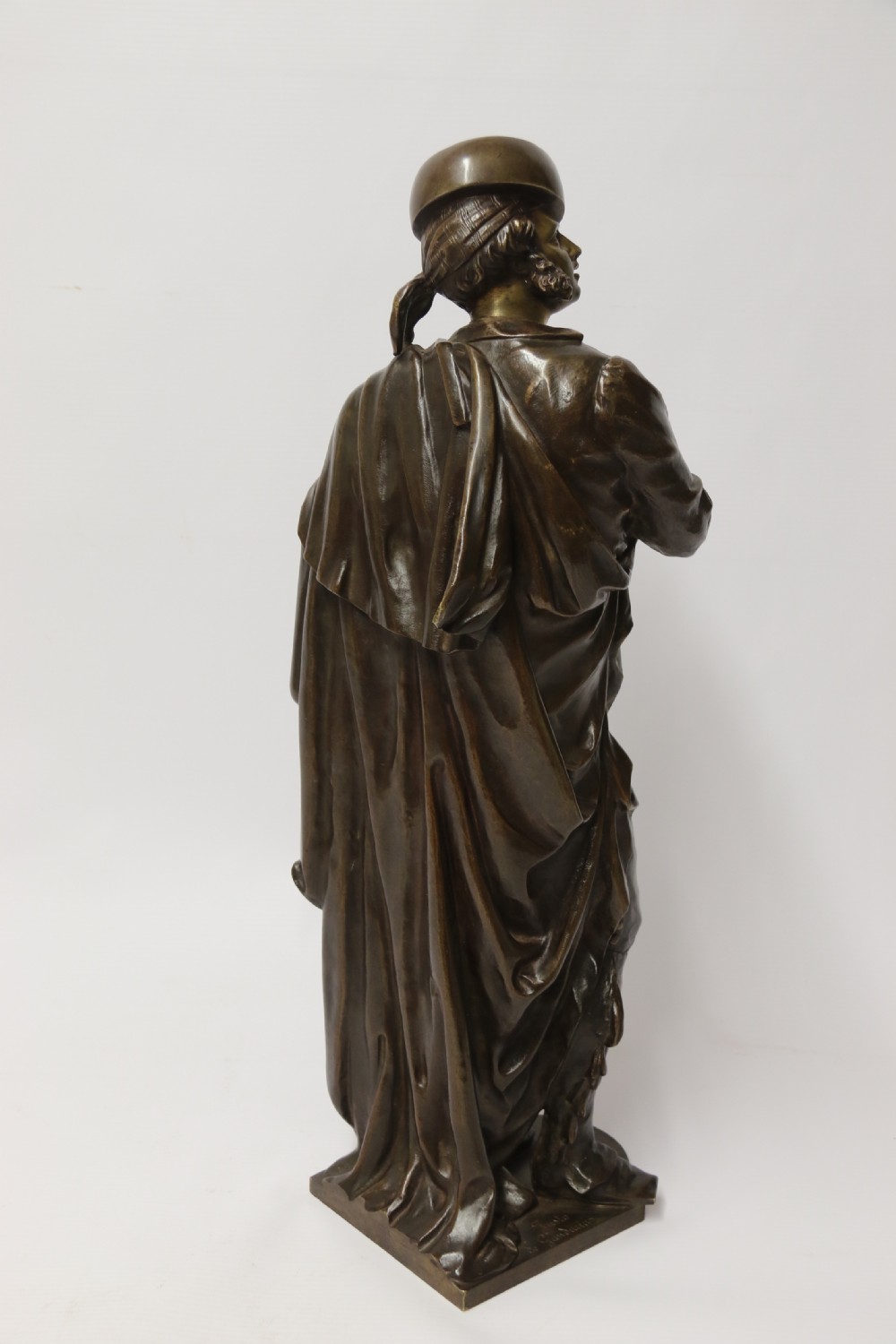 A patinated dark brown bronze sculpture depicting a standing male musician playing a mandolin while wearing a draped coat and headwear. View III