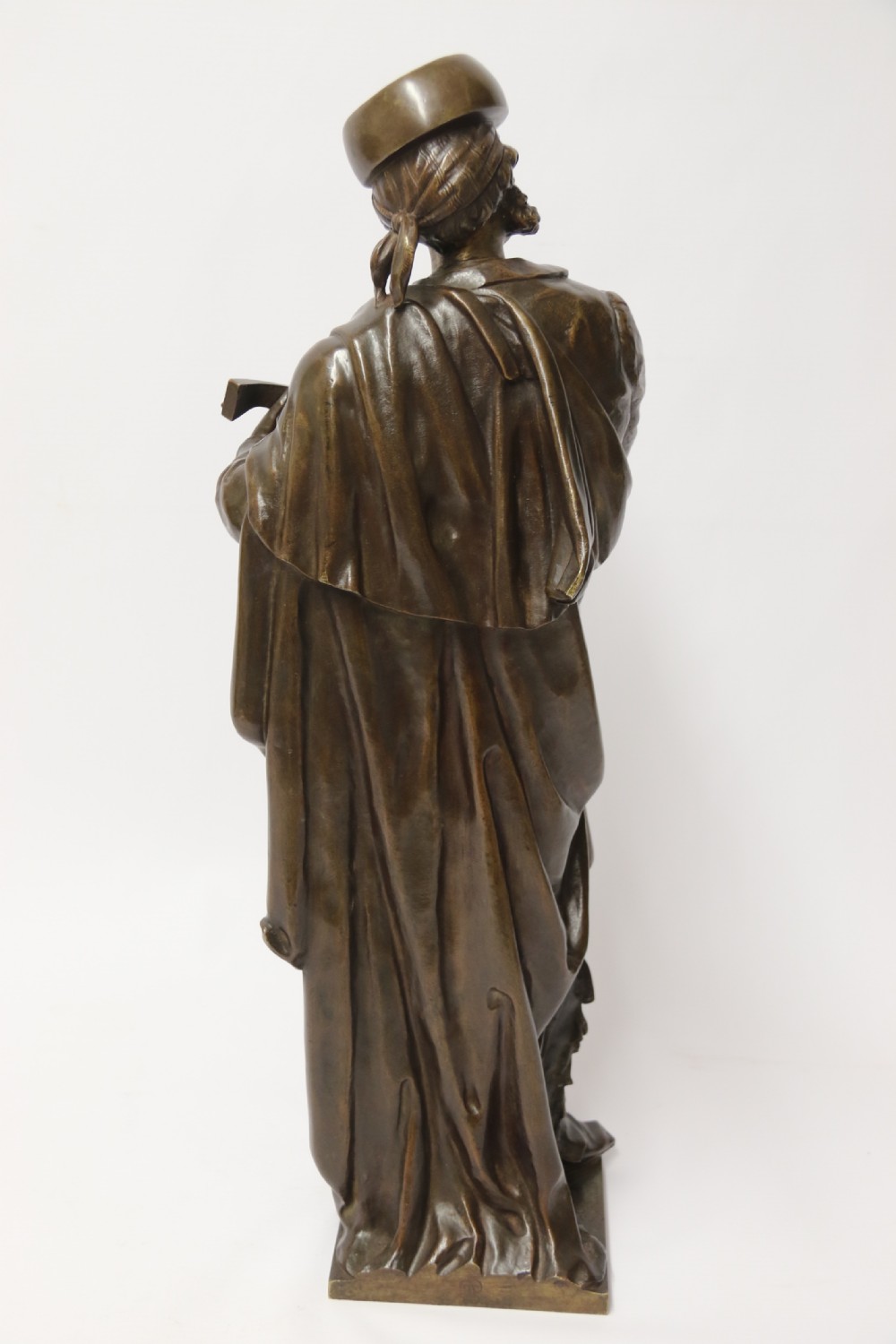 A patinated dark brown bronze sculpture depicting a standing male musician playing a mandolin while wearing a draped coat and headwear. View VII