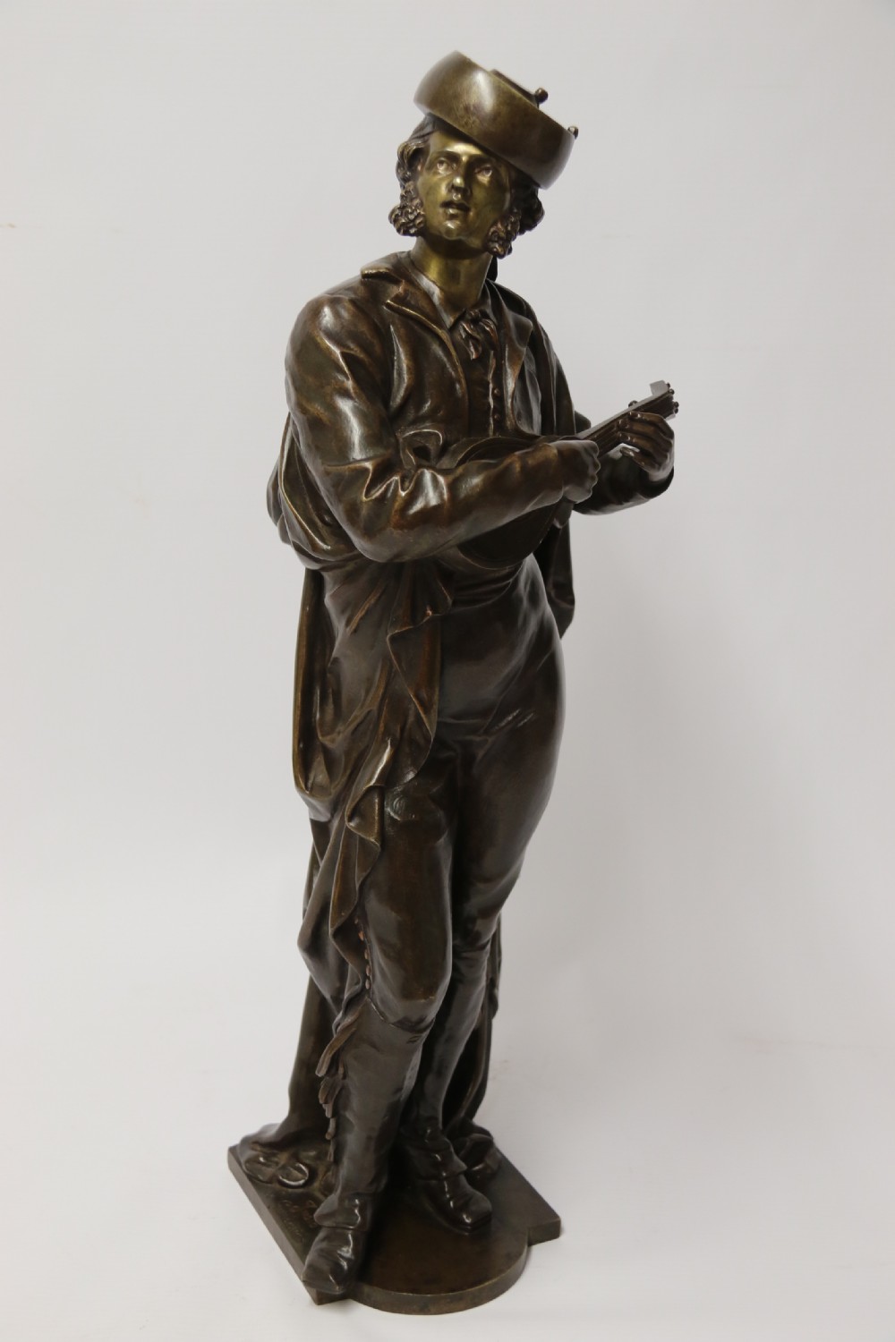 A patinated dark brown bronze sculpture depicting a standing male musician playing a mandolin while wearing a draped coat and headwear. View VIII