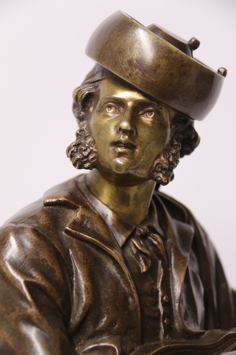 A patinated dark brown bronze sculpture depicting a standing male musician playing a mandolin while wearing a draped coat and headwear. View X