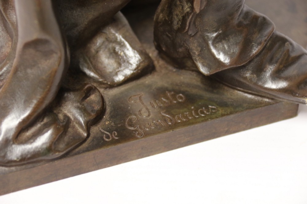 A patinated dark brown bronze sculpture depicting a standing male musician playing a mandolin while wearing a draped coat and headwear. View XV