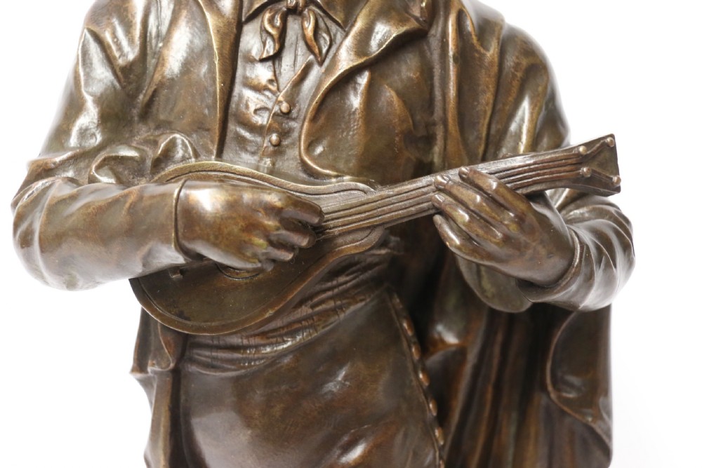 A patinated dark brown bronze sculpture depicting a standing male musician playing a mandolin while wearing a draped coat and headwear. View XVI