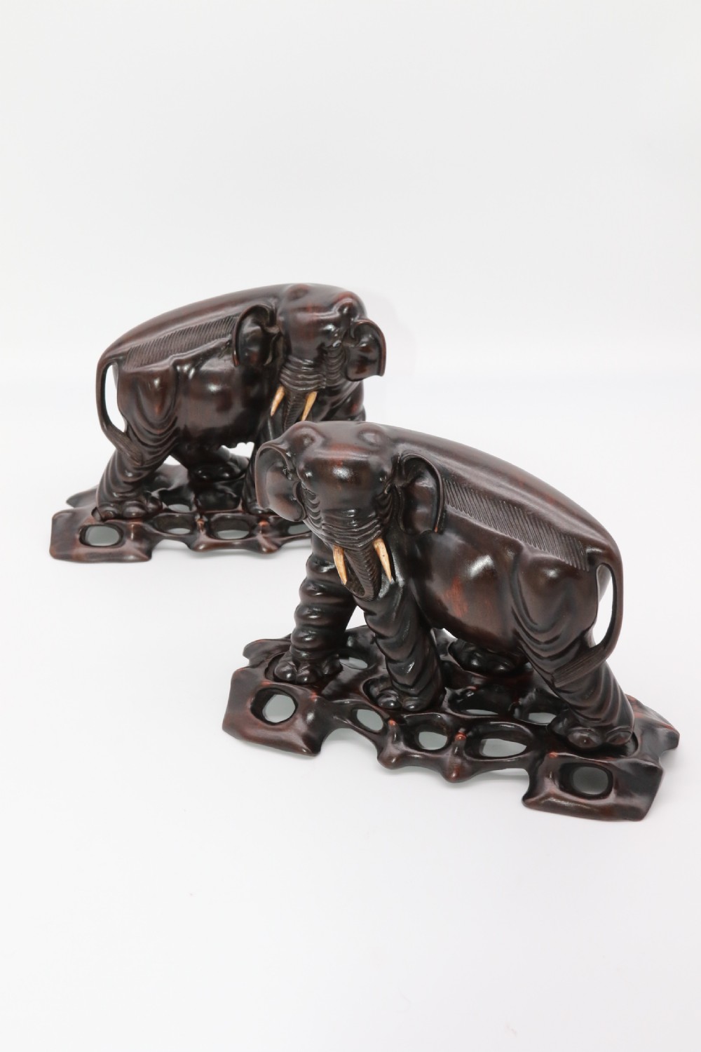 A pair of hand-carved dark hardwood elephant figures standing on pierced wooden bases with exposed tusks. View II