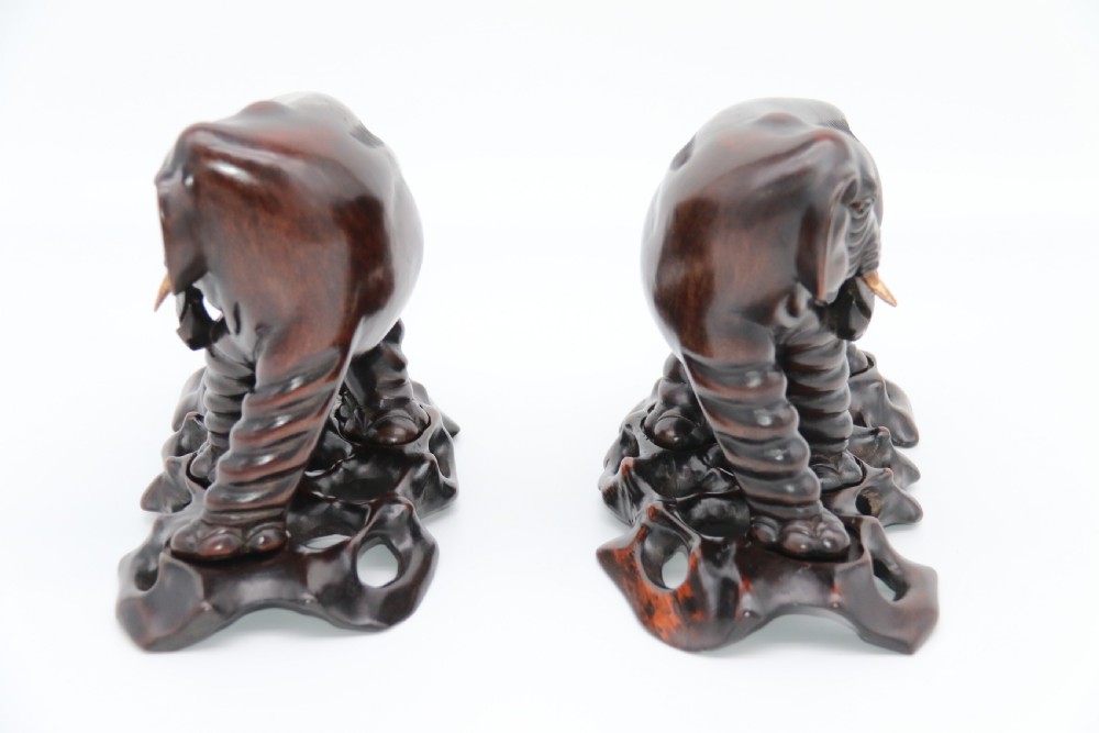 A pair of hand-carved dark hardwood elephant figures standing on pierced wooden bases with exposed tusks. View III