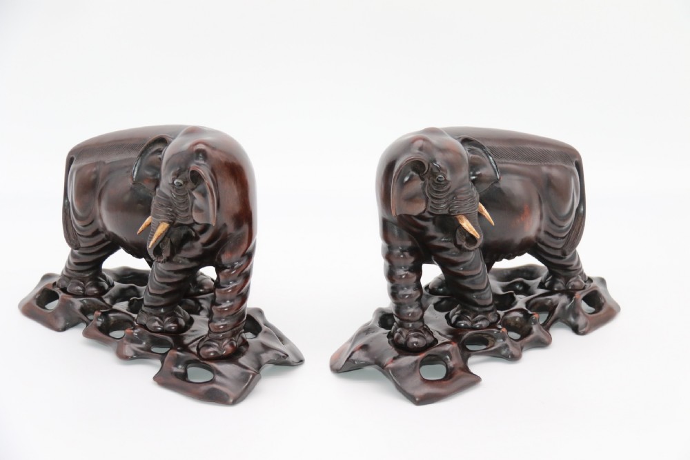 A pair of hand-carved dark hardwood elephant figures standing on pierced wooden bases with exposed tusks. View V