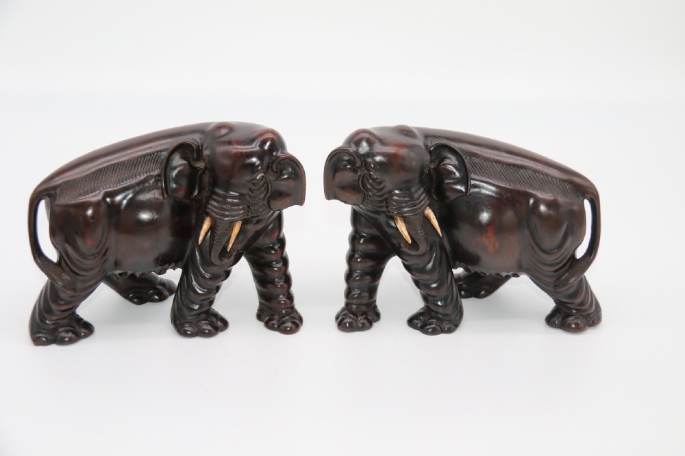 A pair of hand-carved dark hardwood elephant figures standing on pierced wooden bases with exposed tusks. View XXV