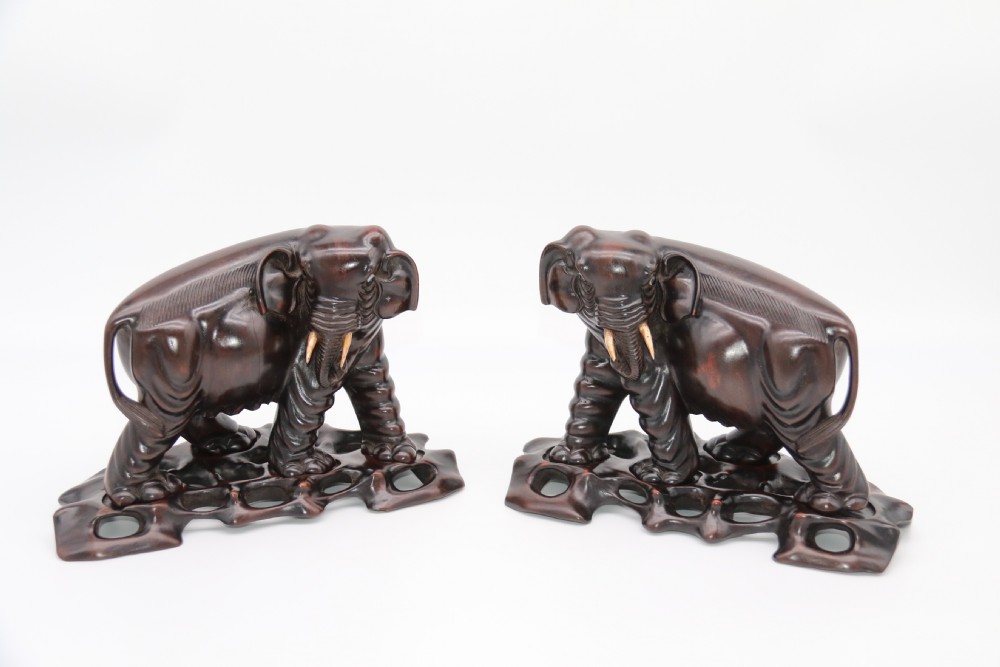 A pair of hand-carved dark hardwood elephant figures standing on pierced wooden bases with exposed tusks.
