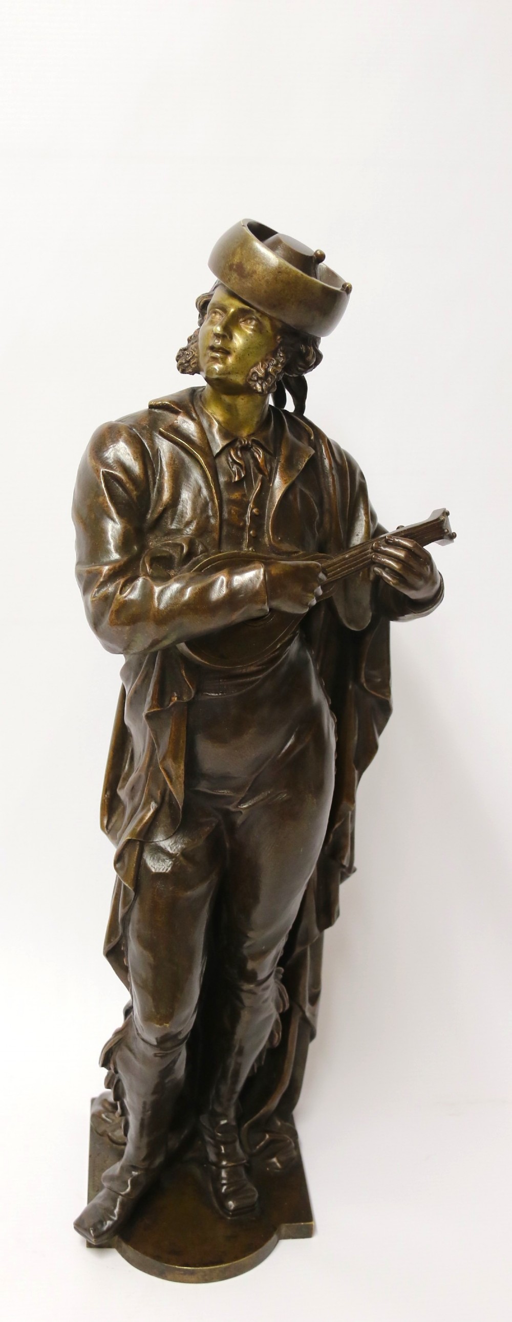 A patinated dark brown bronze sculpture depicting a standing male musician playing a mandolin while wearing a draped coat and headwear.