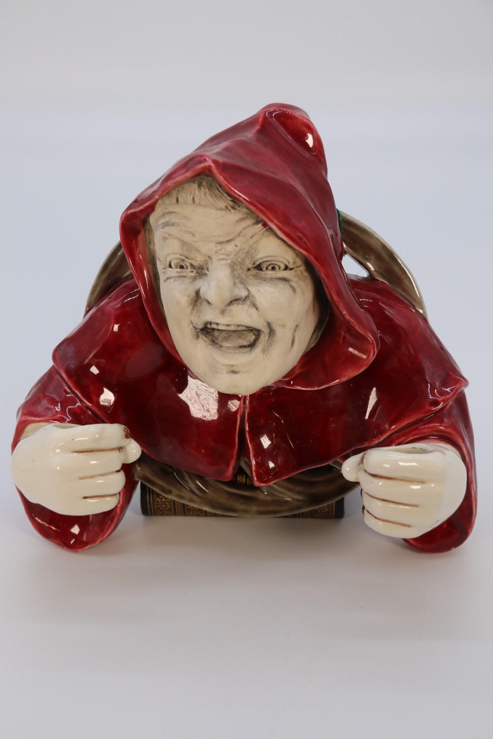 An Edwardian glazed ceramic wall sconce featuring a sculpted hooded figure in a red cowl holding two candle sockets. View II