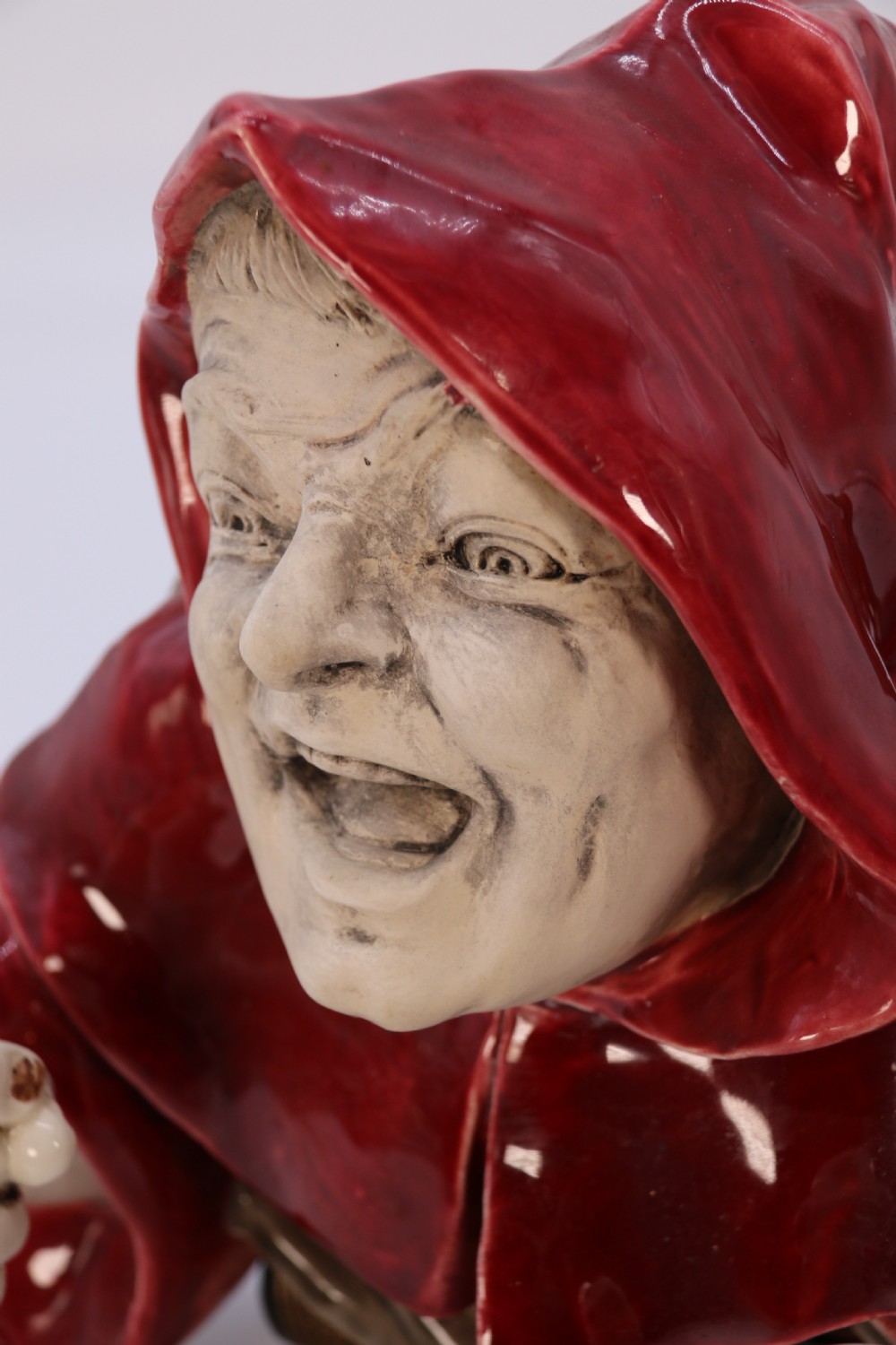 An Edwardian glazed ceramic wall sconce featuring a sculpted hooded figure in a red cowl holding two candle sockets. View III