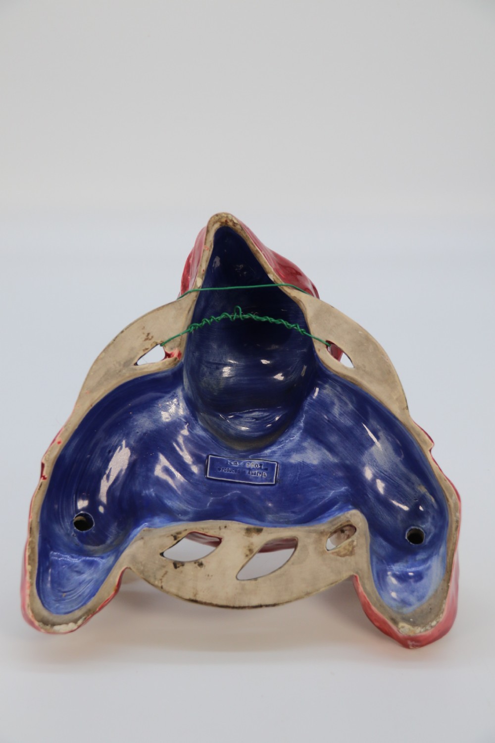An Edwardian glazed ceramic wall sconce featuring a sculpted hooded figure in a red cowl holding two candle sockets. View IV