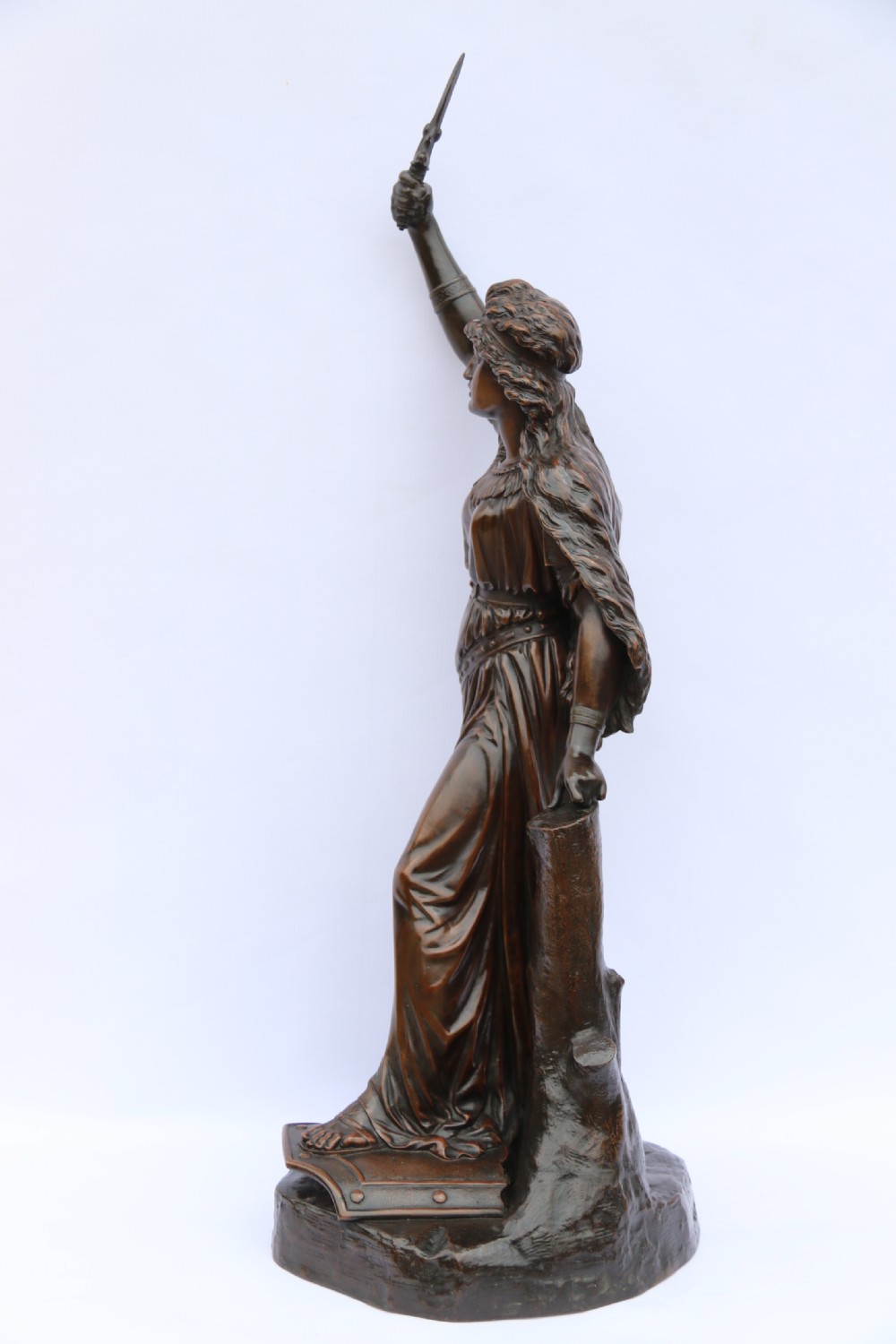 A 19th-century dark patinated bronze sculpture depicting Queen Boadicea in draped robes raising a dagger in her right hand while standing on a rocky base. View III