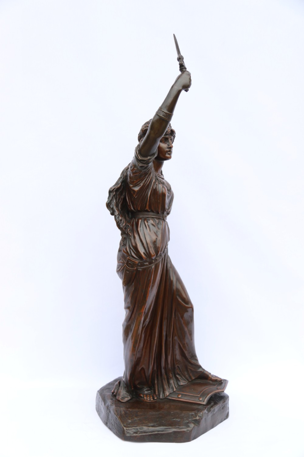 A 19th-century dark patinated bronze sculpture depicting Queen Boadicea in draped robes raising a dagger in her right hand while standing on a rocky base. View VIII