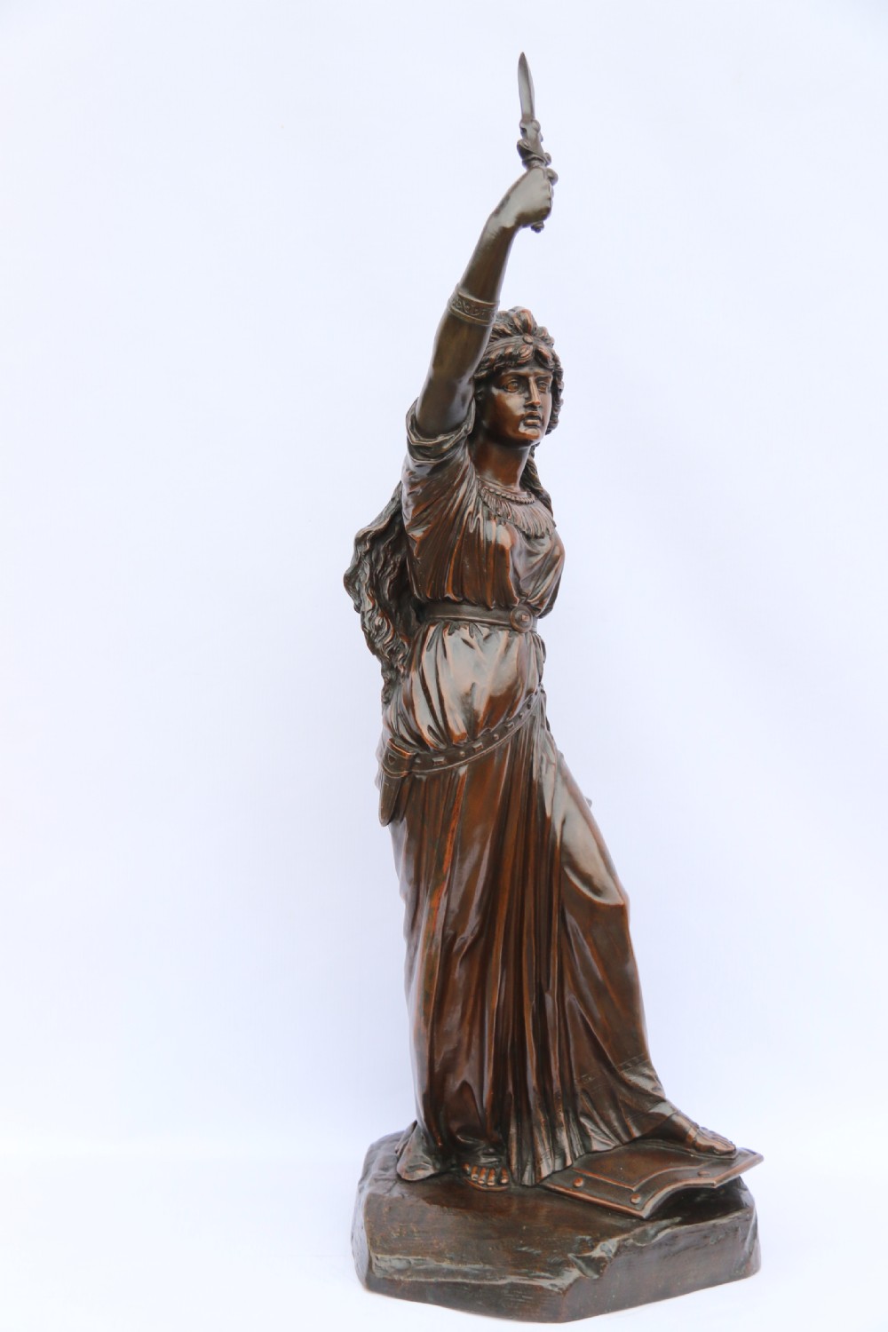 A 19th-century dark patinated bronze sculpture depicting Queen Boadicea in draped robes raising a dagger in her right hand while standing on a rocky base. View XI
