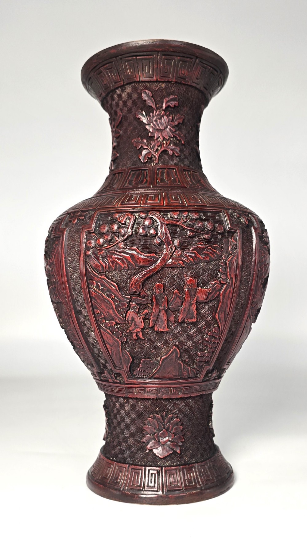 A baluster-shaped red cinnabar lacquer vase decorated with relief carvings of figures in a landscape surrounded by floral and geometric borders.