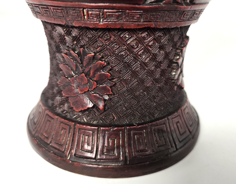 A baluster-shaped red cinnabar lacquer vase decorated with relief carvings of figures in a landscape surrounded by floral and geometric borders. View XVII