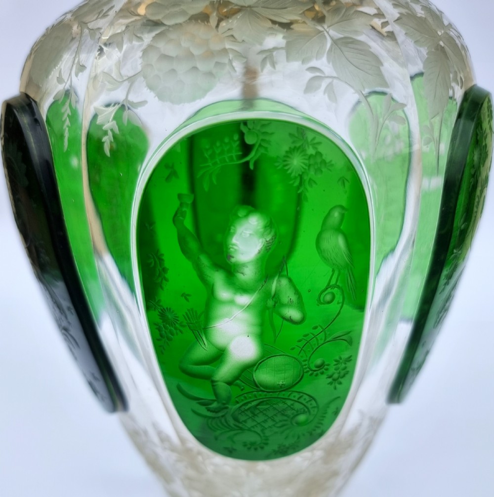 A clear glass claret jug featuring green overlay panels etched with floral motifs, topped with a metal collar, spout, lid, and geometric handle. View X
