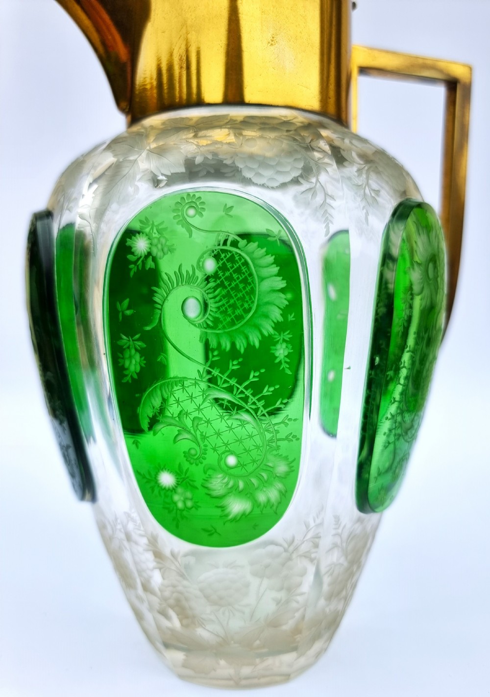 A clear glass claret jug featuring green overlay panels etched with floral motifs, topped with a metal collar, spout, lid, and geometric handle. View XI