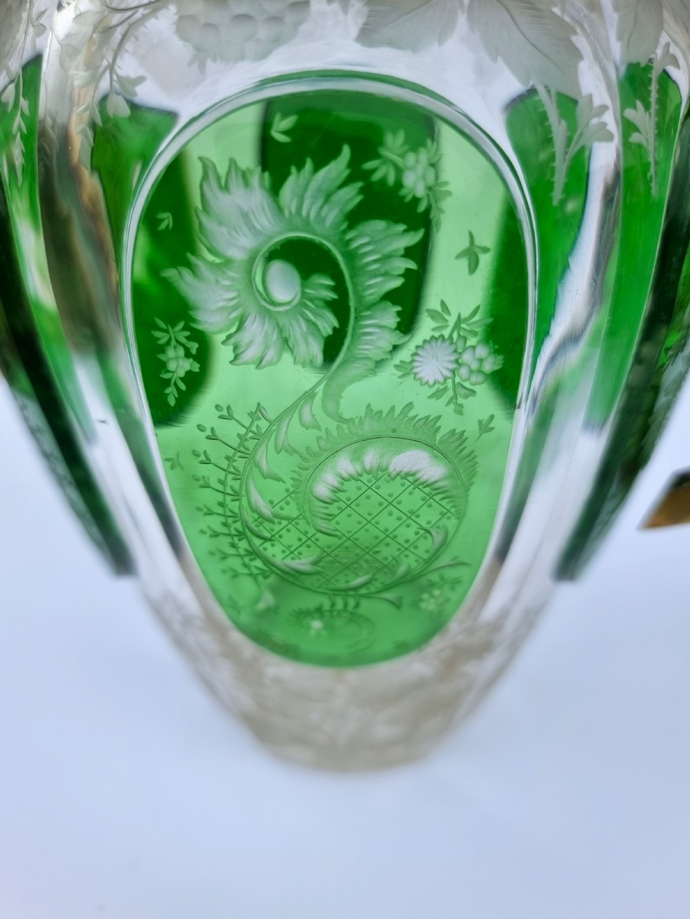 A clear glass claret jug featuring green overlay panels etched with floral motifs, topped with a metal collar, spout, lid, and geometric handle. View XII