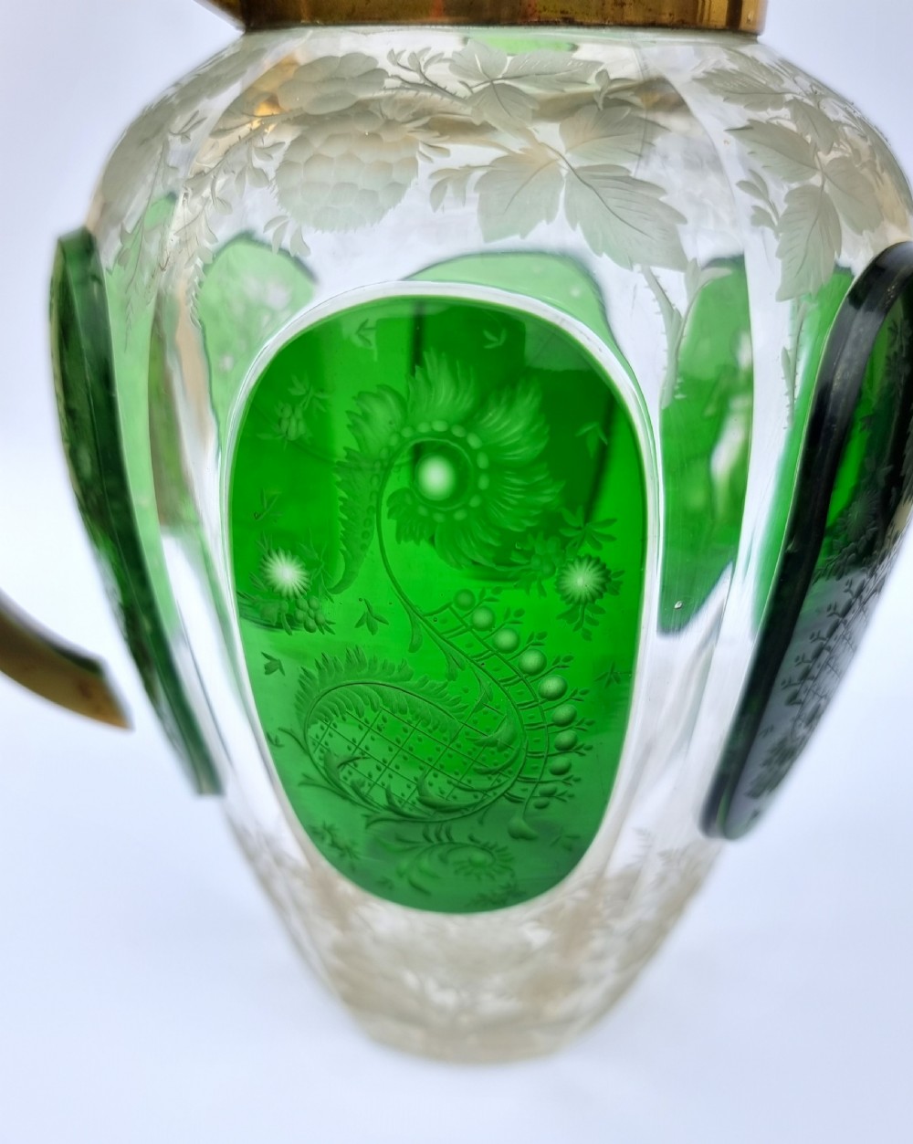 A clear glass claret jug featuring green overlay panels etched with floral motifs, topped with a metal collar, spout, lid, and geometric handle. View XIII