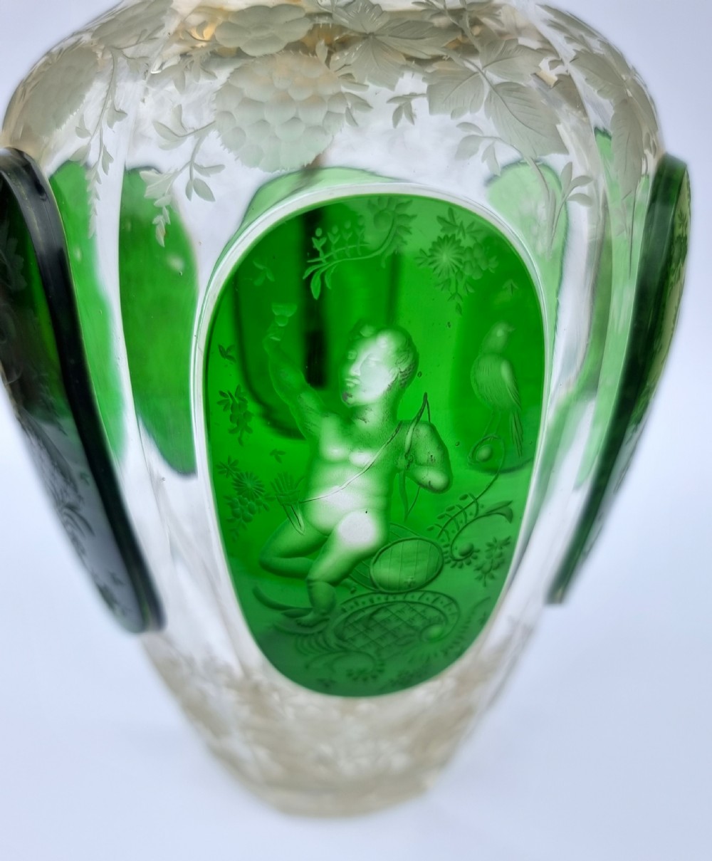A clear glass claret jug featuring green overlay panels etched with floral motifs, topped with a metal collar, spout, lid, and geometric handle. View XV